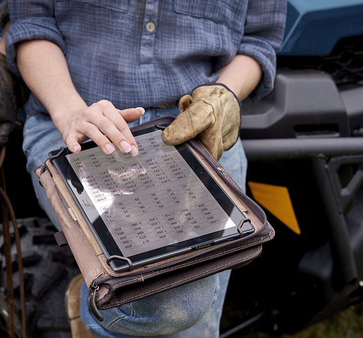 Woman outdoors on ATV holding a tablet showcasing a table of data.